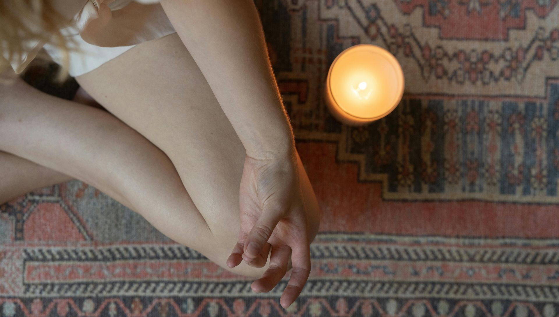 Person sitting with a lit candle on a patterned rug.