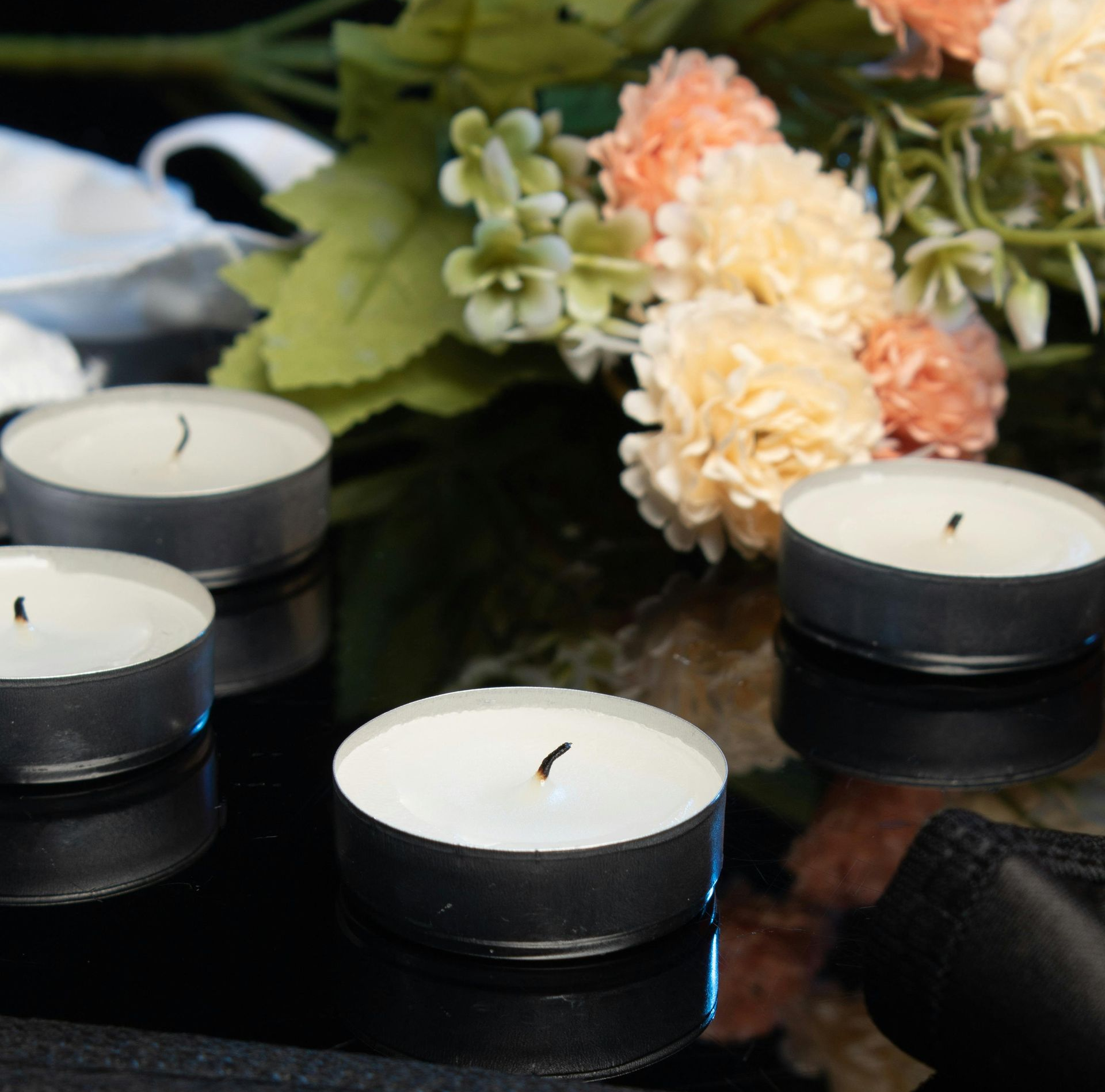 Four lit tealight candles with flowers in the background.