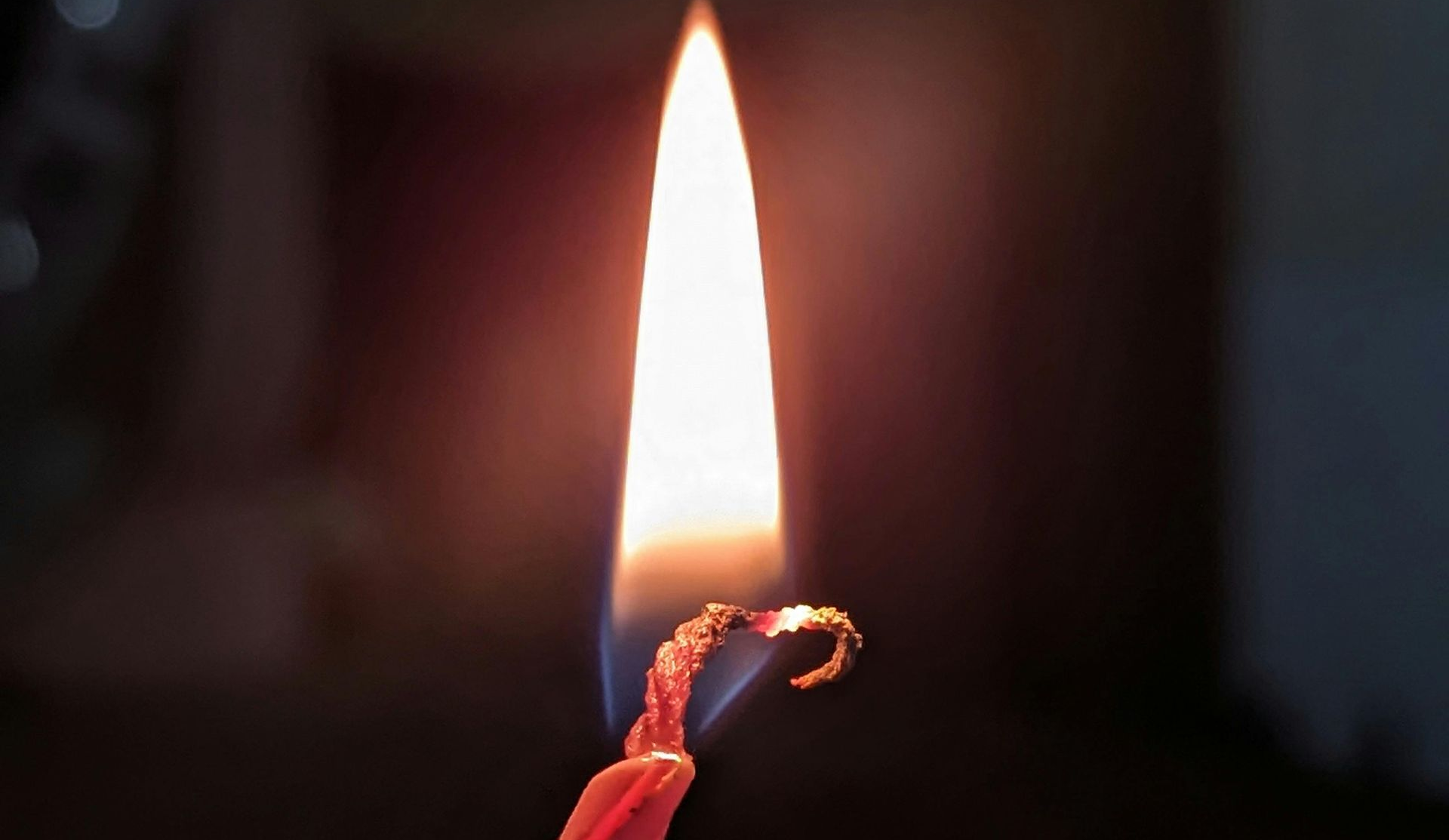 Lit red candle flame burning brightly against a dark background.
