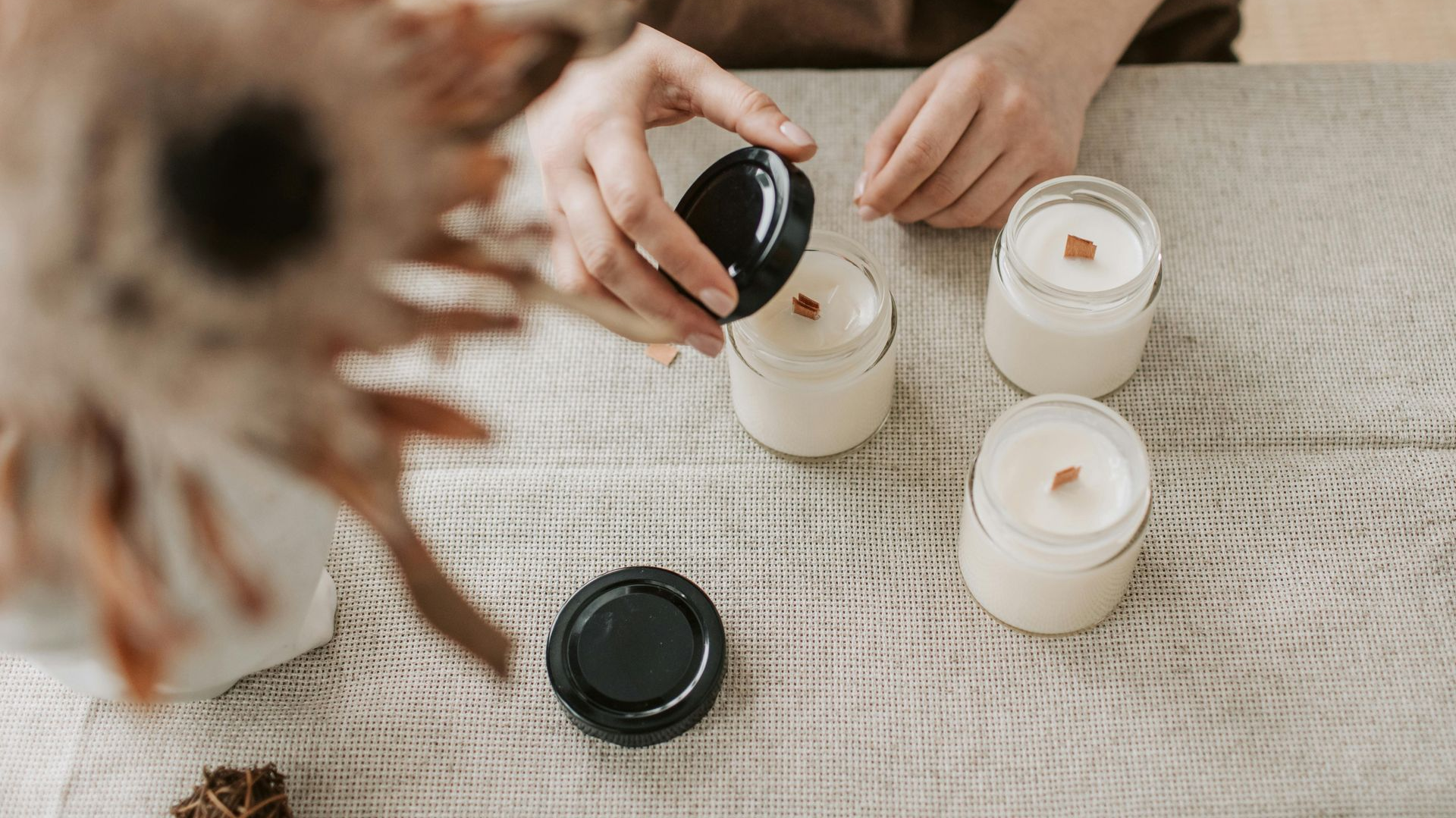 Person placing lid on a candle jar with others on a table.