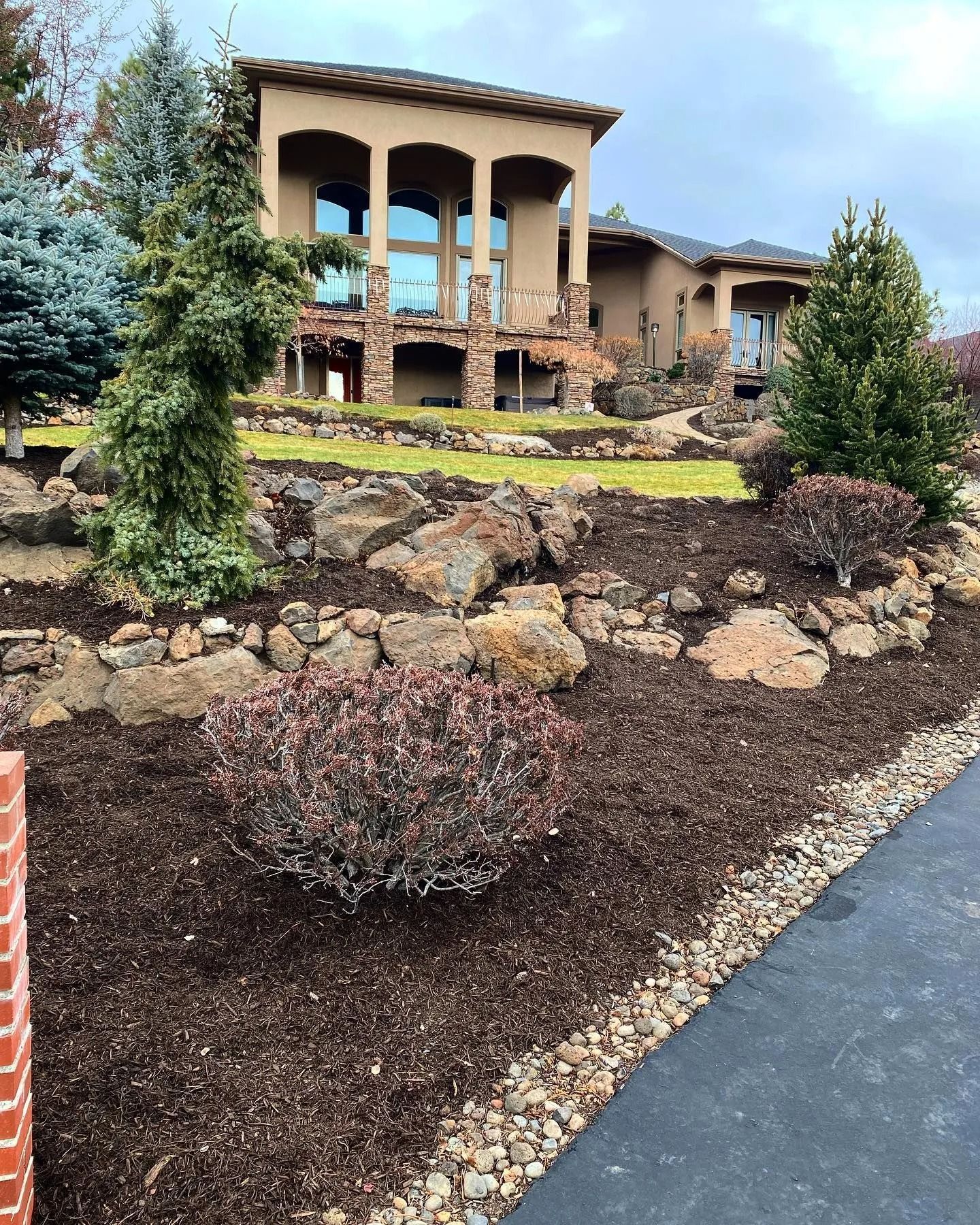 A tan stucco house with a balcony and a landscaped yard with rocks and mulch.