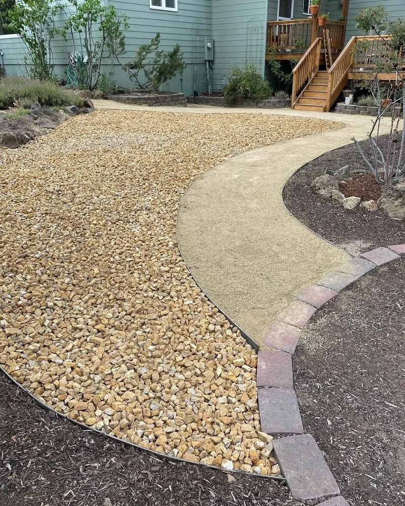 Gravel paths in a garden. One path is light tan, the other is darker. A house and wooden deck are in the background.