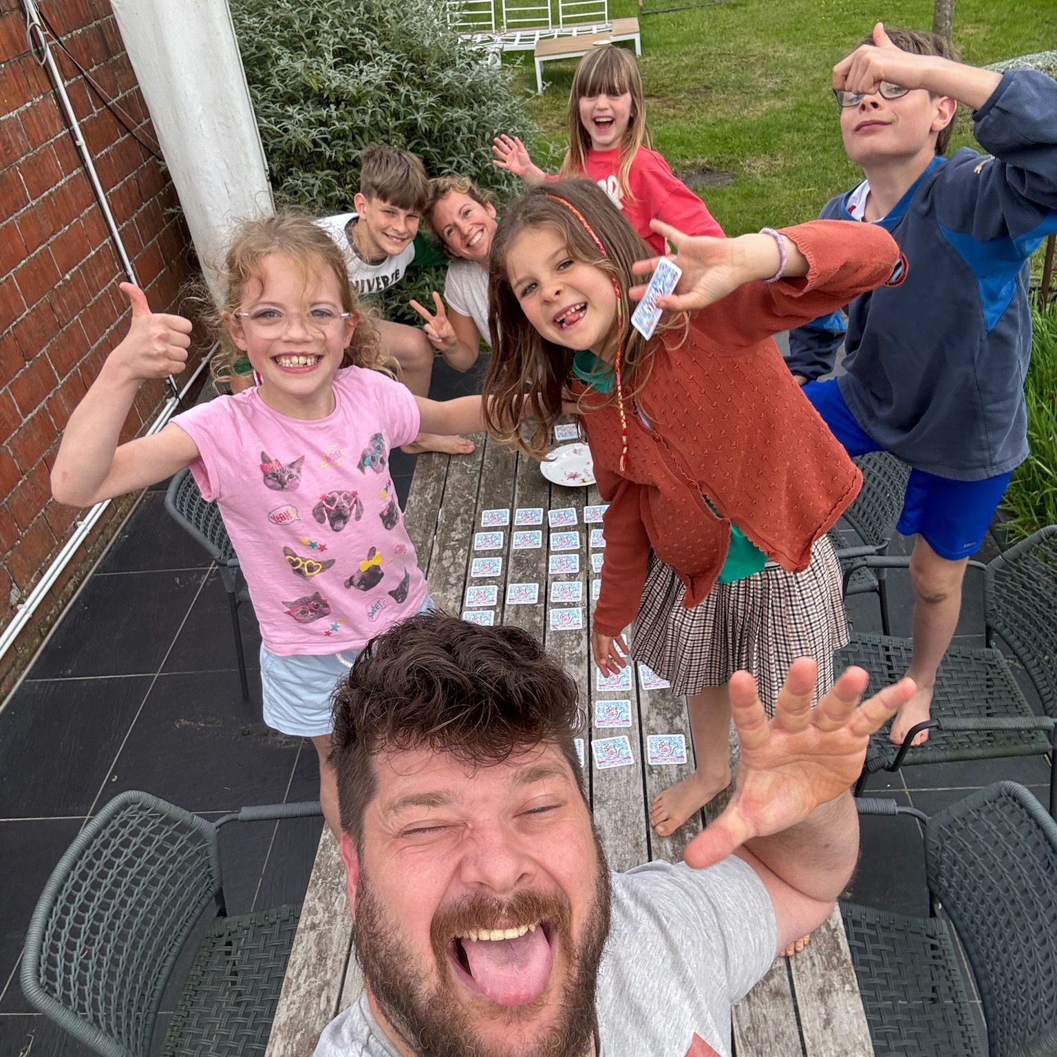 Een man neemt een selfie met een groep kinderen die rond een tafel zitten.