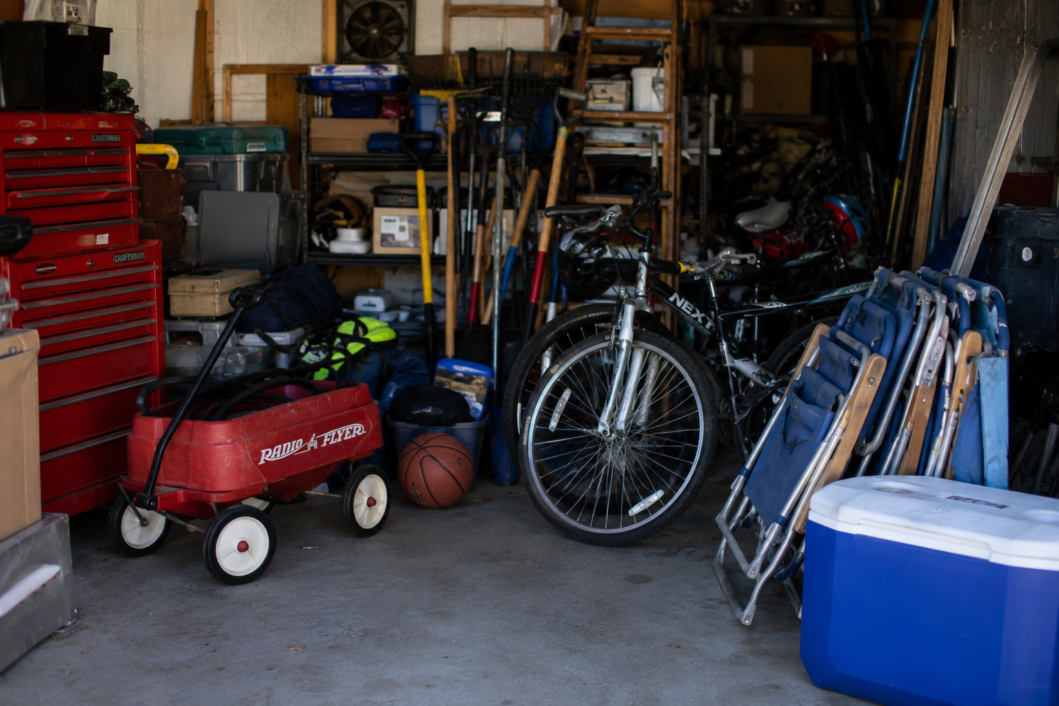 Cluttered garage with tools, a red wagon, a basketball, bikes, and folded chairs stacked tightly together