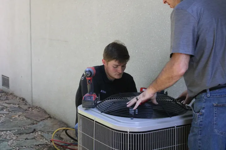 A man is working on an air conditioner while another man looks on.