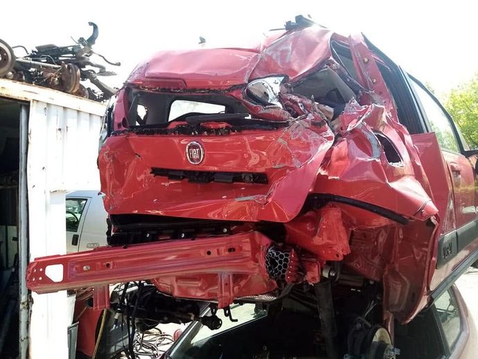 Auto rossa gravemente danneggiata, con parte anteriore e posteriore ammaccate, mostrata in un ambiente esterno devastato.
