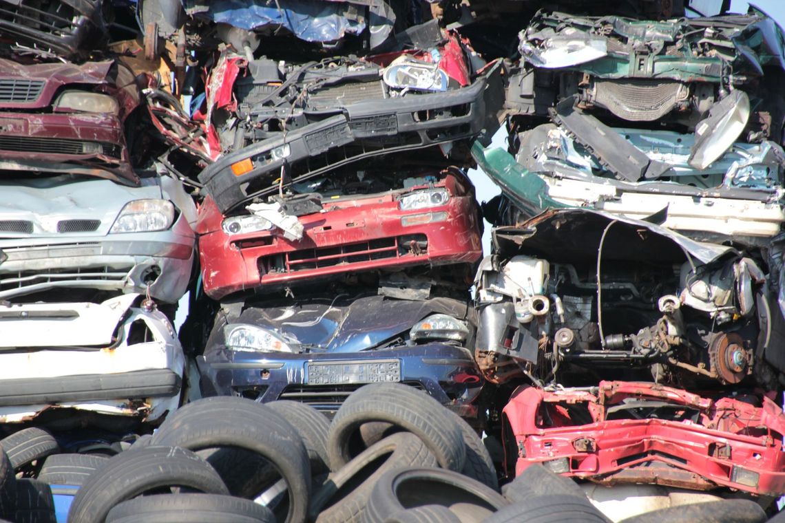 Cumulo di auto schiacciate e accatastate in una discarica, con pneumatici in primo piano.