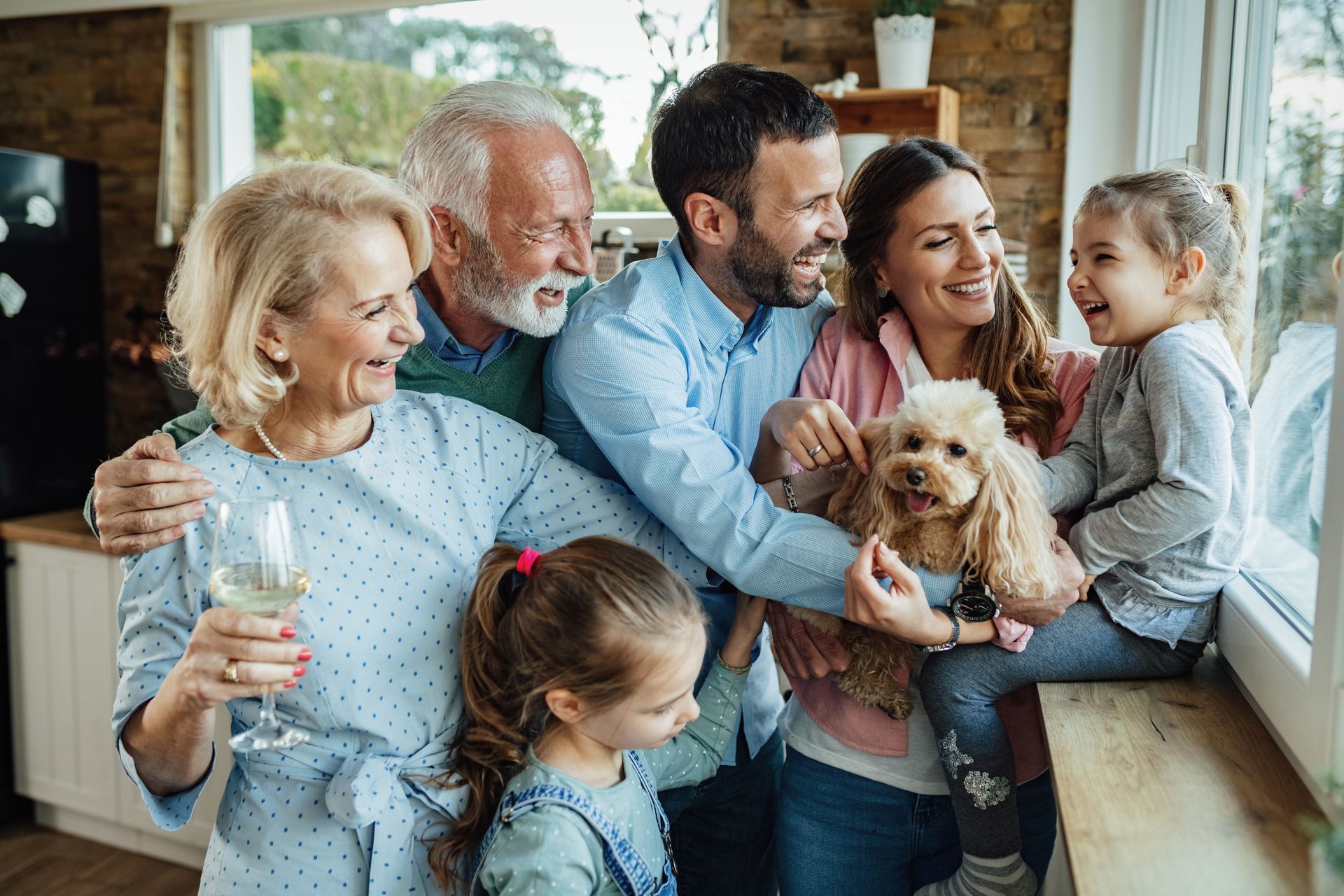 Family, including two children and a dog, smiles while gathered near a window.