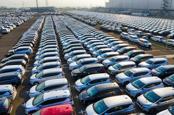 Rows of parked cars in a large outdoor lot, mostly white and blue vehicles seen from above.