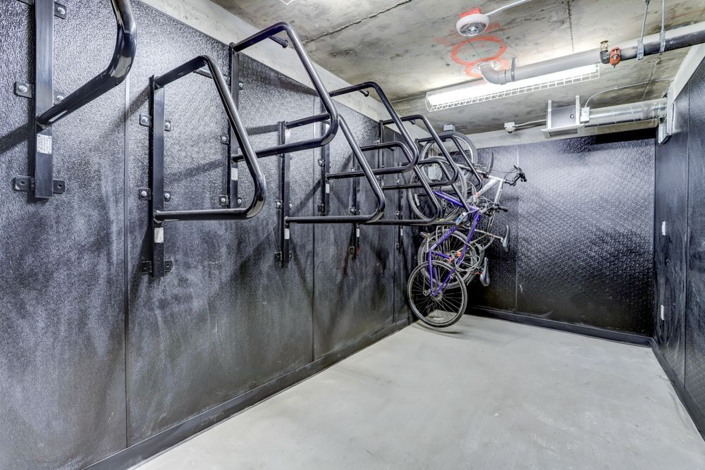 Bike storage room with multiple wall-mounted hanging racks and a few bicycles against black padded walls.