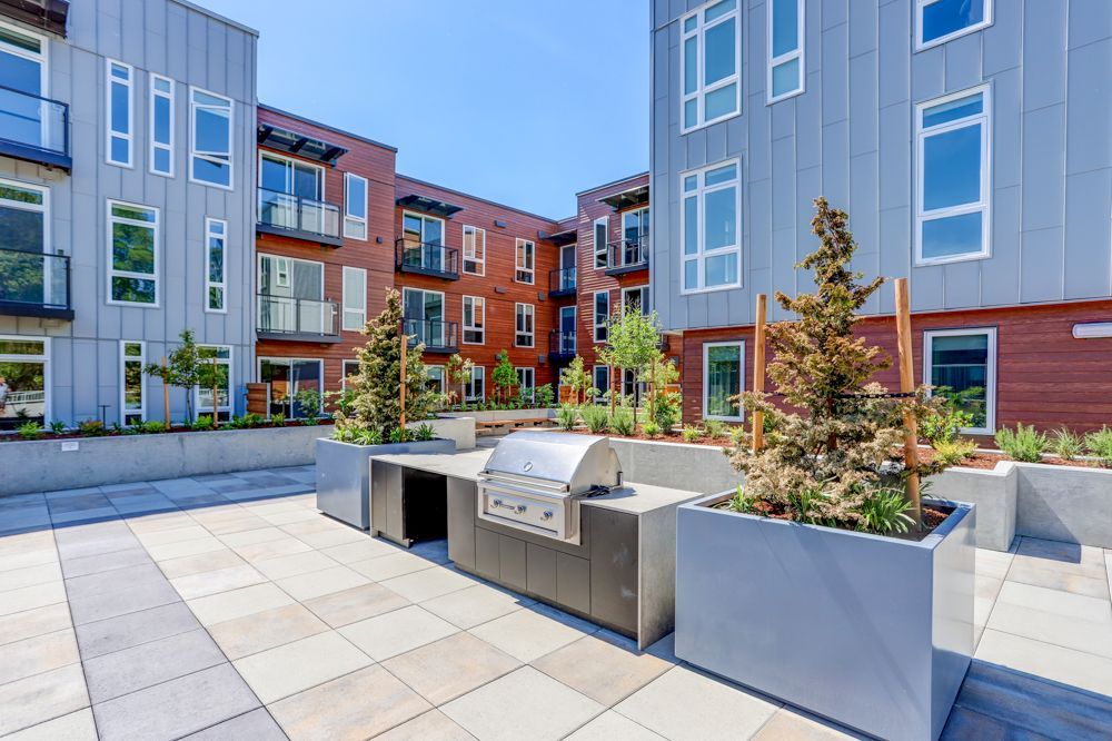 Modern apartment courtyard with planters, benches, and a grill between multistory buildings