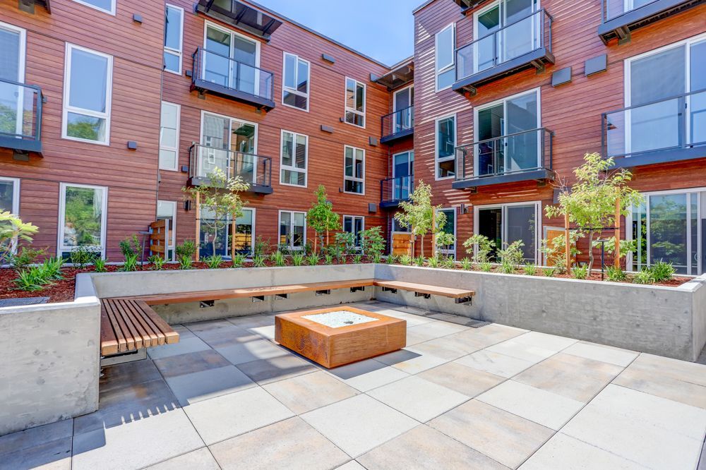 Modern apartment courtyard with benches, raised planters, and potted trees on a paved patio