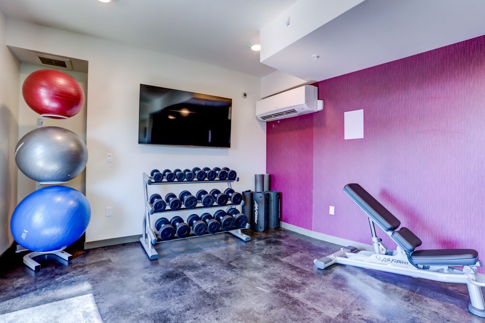 Gym room with exercise balls, dumbbells, wall TV, and adjustable bench on a purple accent wall