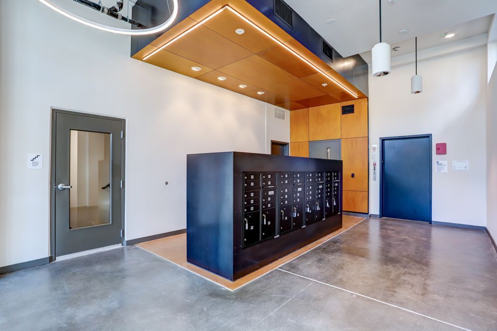 Modern apartment lobby with mailboxes, concrete floor, and wood-accented ceiling over a central desk area