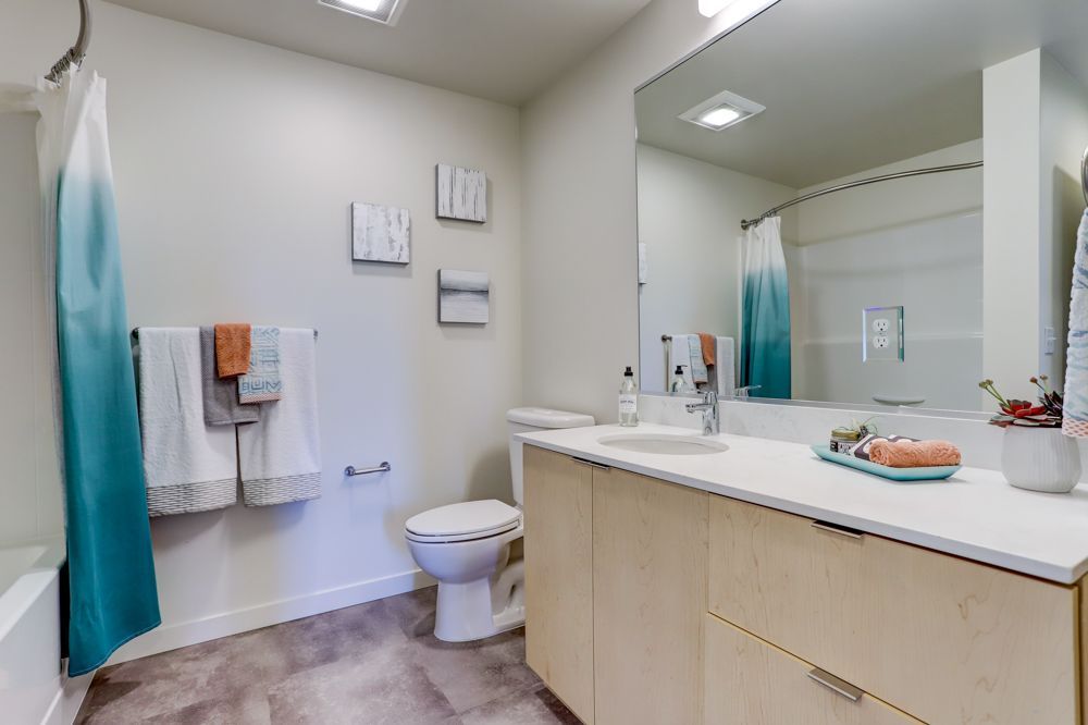 Modern bathroom with white walls, beige vanity, large mirror, toilet, and blue shower curtain