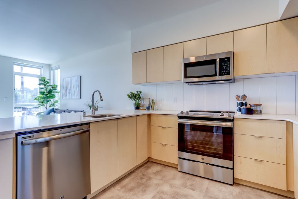 Modern kitchen with light wood cabinets, stainless steel appliances, and a large window by the sink