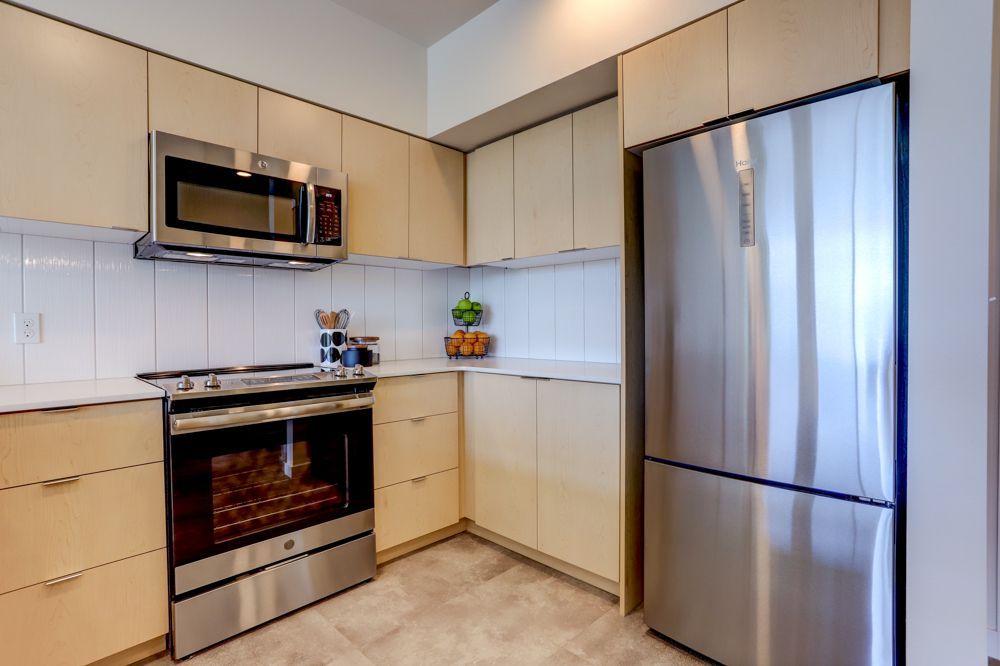 Modern kitchen with stainless steel appliances, beige cabinets, and light tile flooring