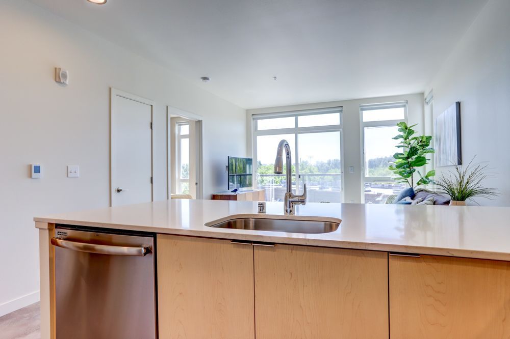 Modern kitchen with island, sink, light wood cabinetry, and a bright windowed dining area