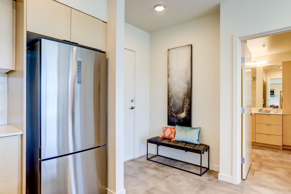 Modern hallway with stainless steel refrigerator, bench, and bathroom vanity in the background