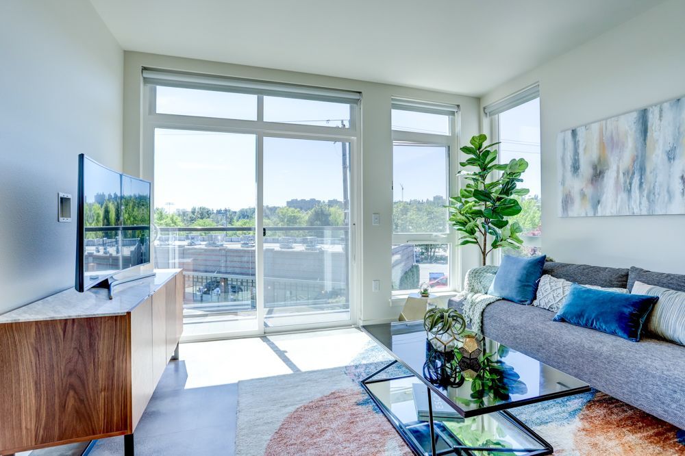 Bright modern living room with large windows, gray sofa, glass coffee table, and balcony view