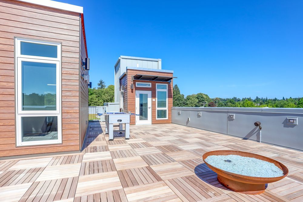 Rooftop deck with wood flooring, seating area, and small modern rooftop structure under blue sky