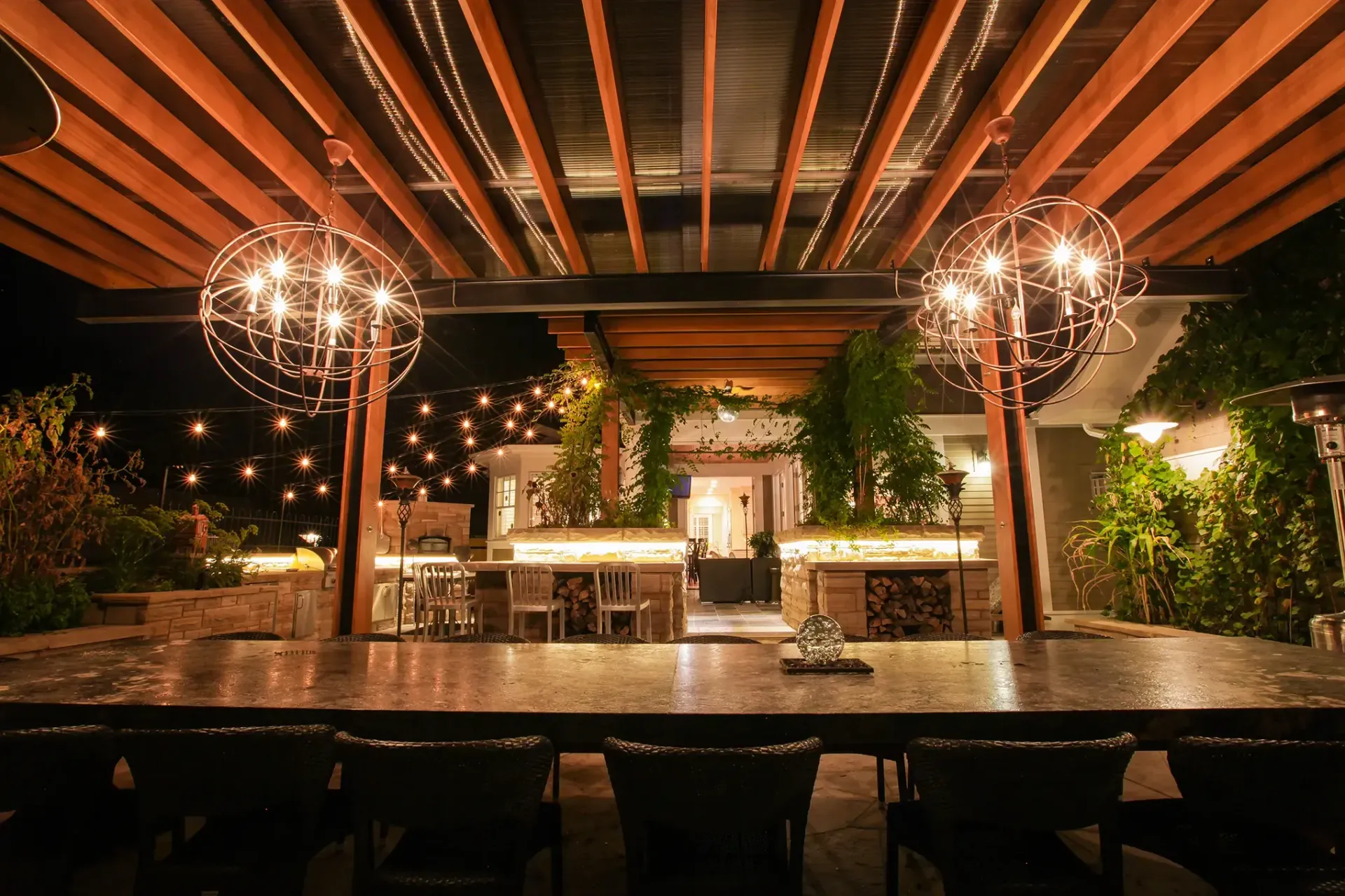 A dining room with a long table and chairs under a pergola at night.