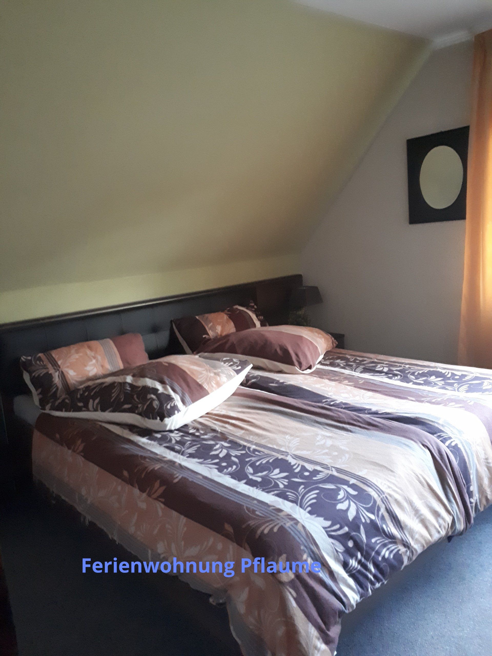 Slaapkamer met een bed, een dekbed met patroon, kussens en een zwart hoofdbord onder een schuin plafond.