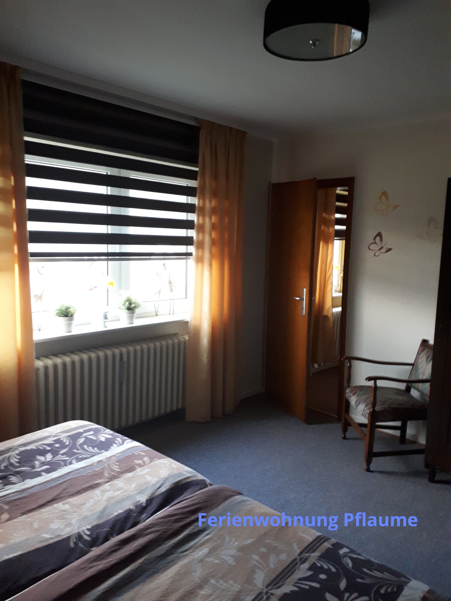 Slaapkamer met een bed, raam met jaloezieën en gordijnen, stoel en kast. Warm zonlicht.