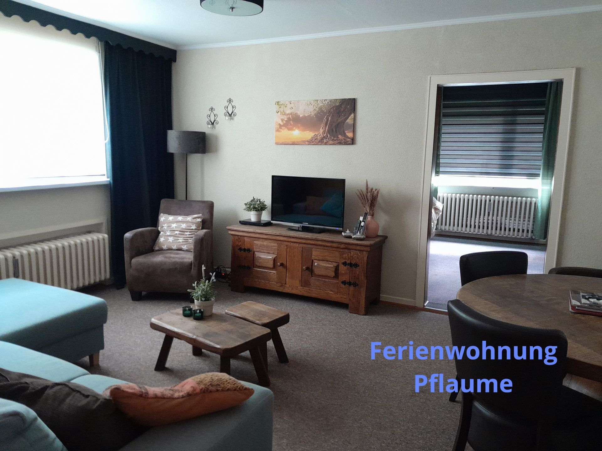 Woonkamer met blauwe bank, houten kast en deur naar een balkon. Label 