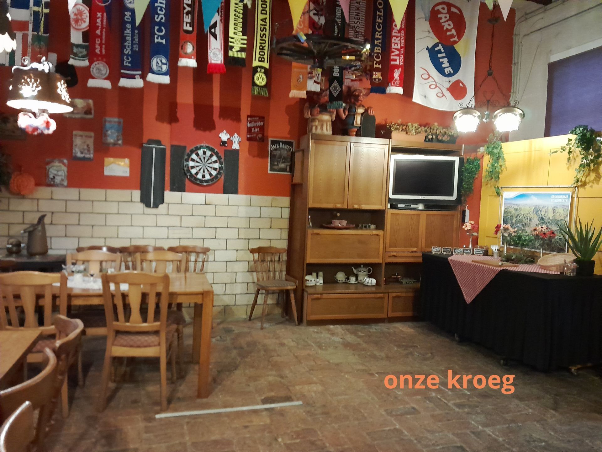 Interieur van een pub met houten meubels, een dartbord en sportscarfs die aan het plafond hangen.