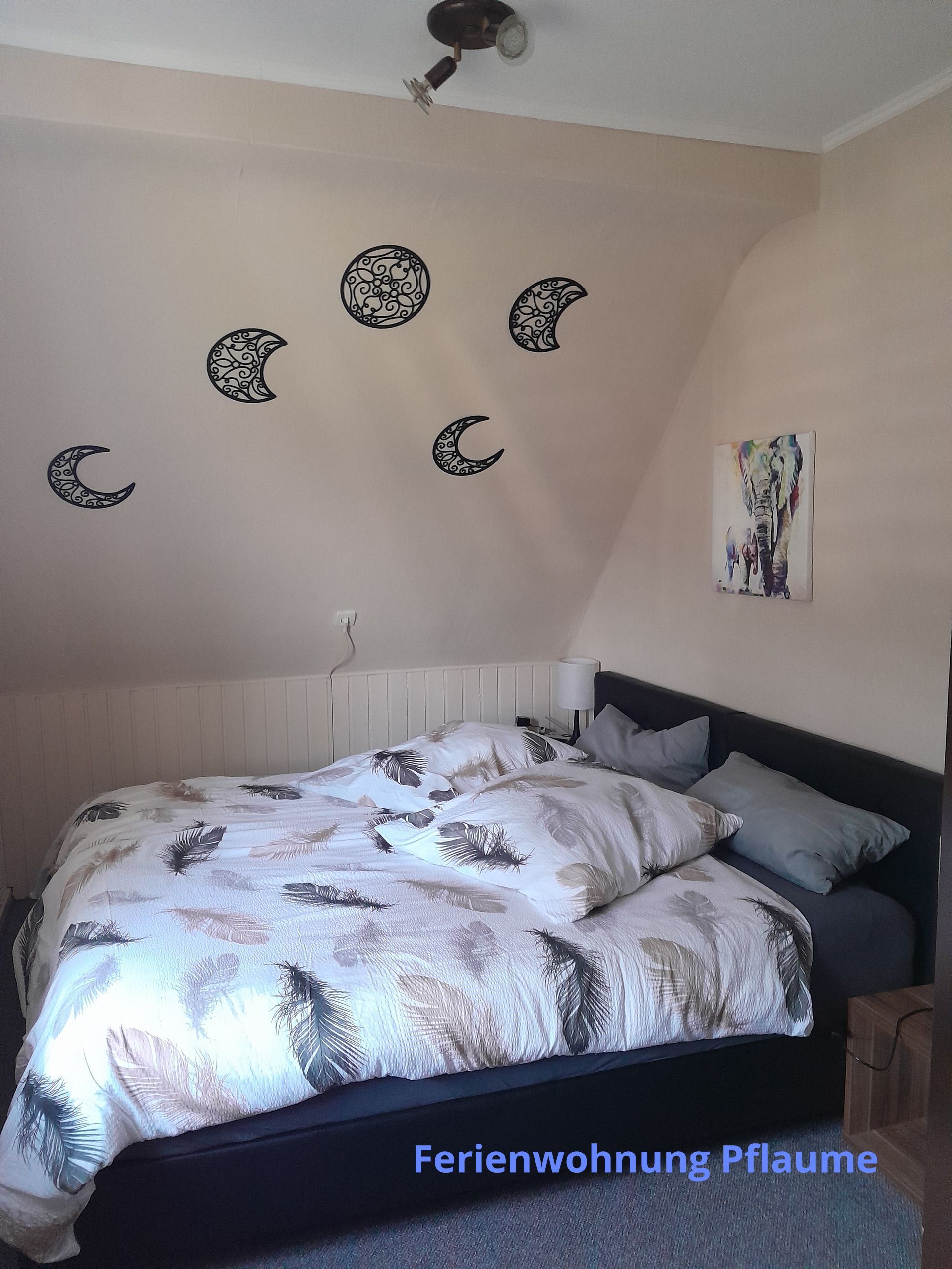 Slaapkamer met bed, muurstickers met maanfasen en kleine kunstwerken.