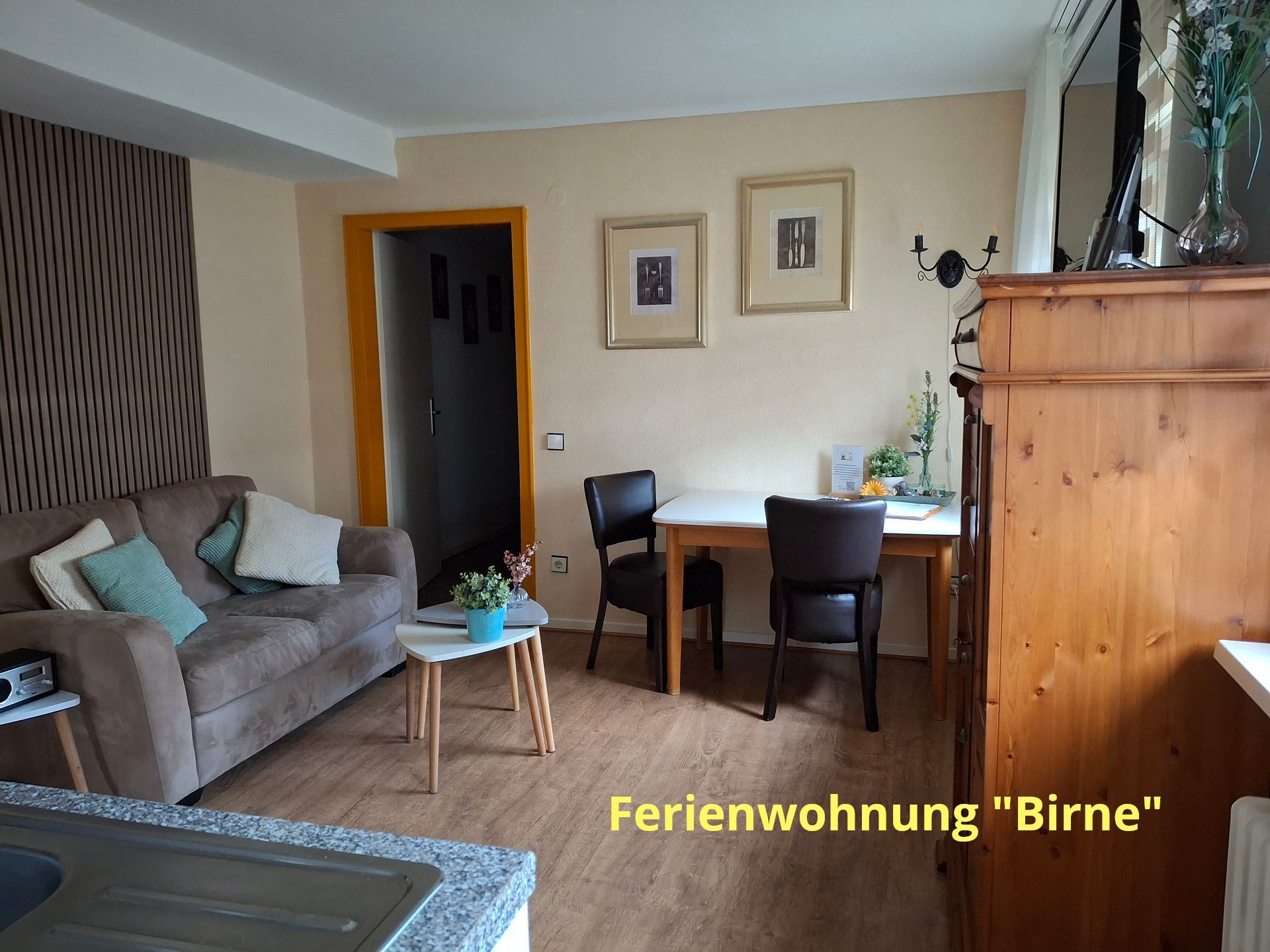Woonkamer met bruine bank, bijzettafel, eettafel met stoelen en houten kast; tekst 