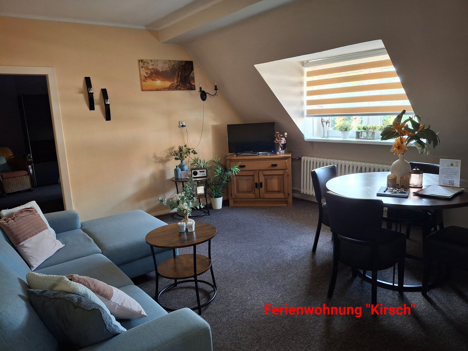 Gezellig appartementinterieur met een blauwe bank, ronde tafel, tv en raam met jaloezieën.