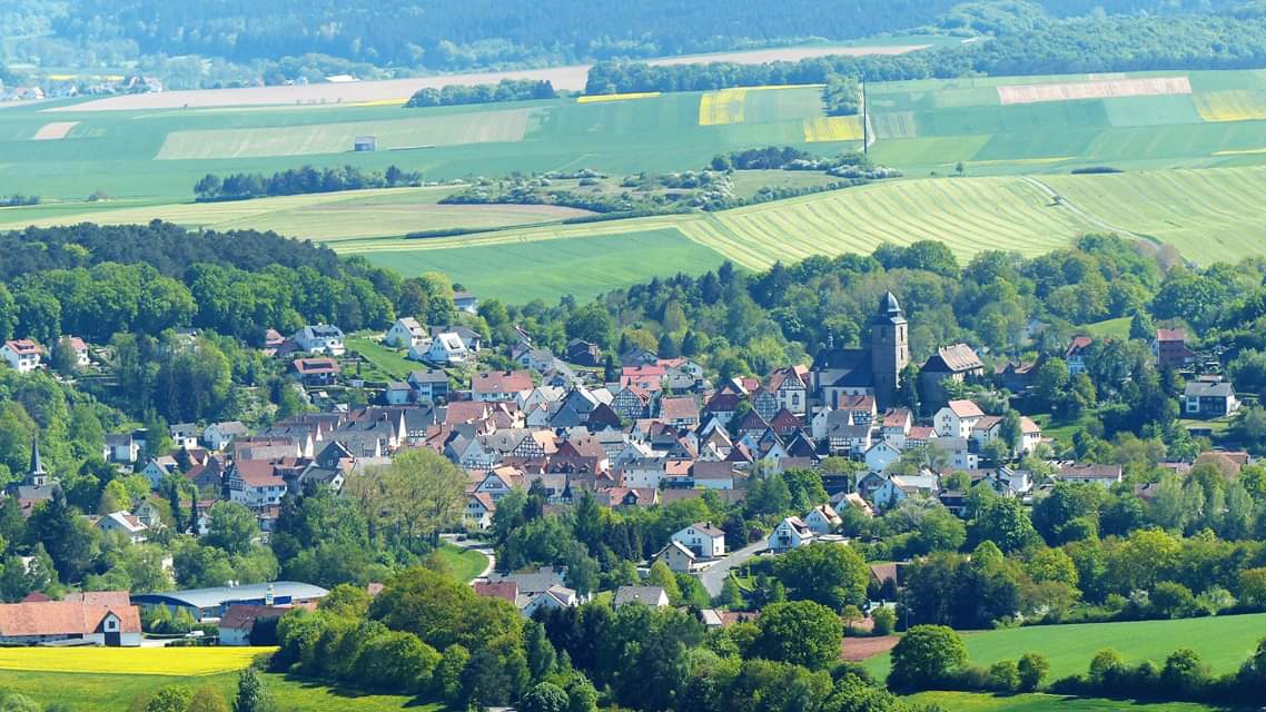 Bovenaanzicht van Naumburg Hessen met gebouwen met rode daken, omgeven door groene velden en bomen.