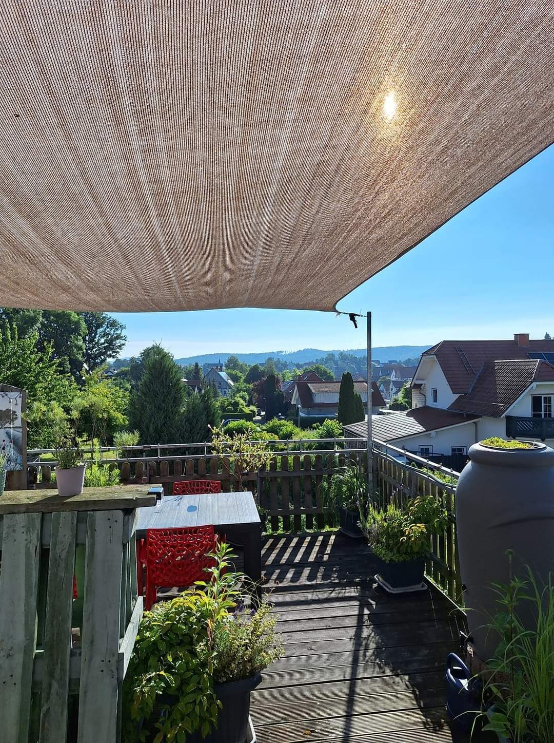 Terras met zonnescherm, met uitzicht op een voorstedelijk landschap op een zonnige dag.