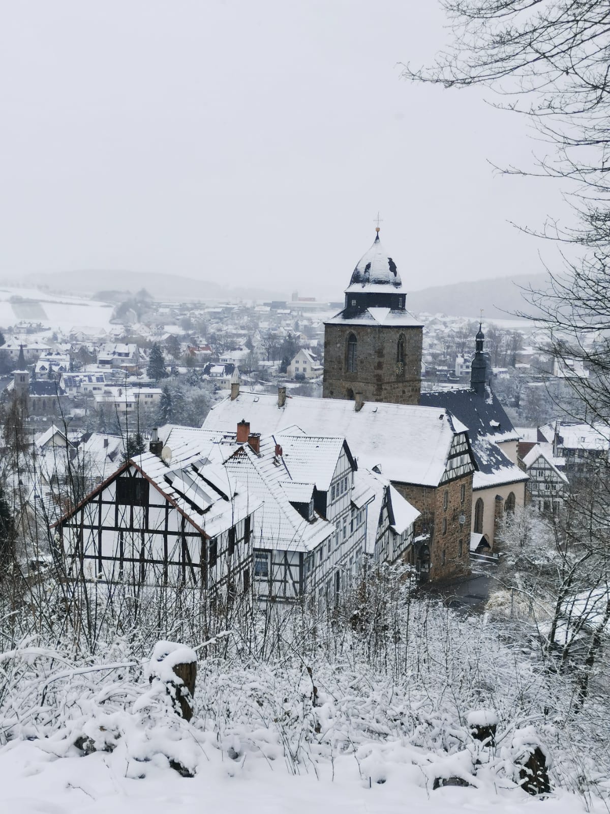 Een besneeuwd uitzicht op een stadje met vakwerkgebouwen en een stenen kerktoren.