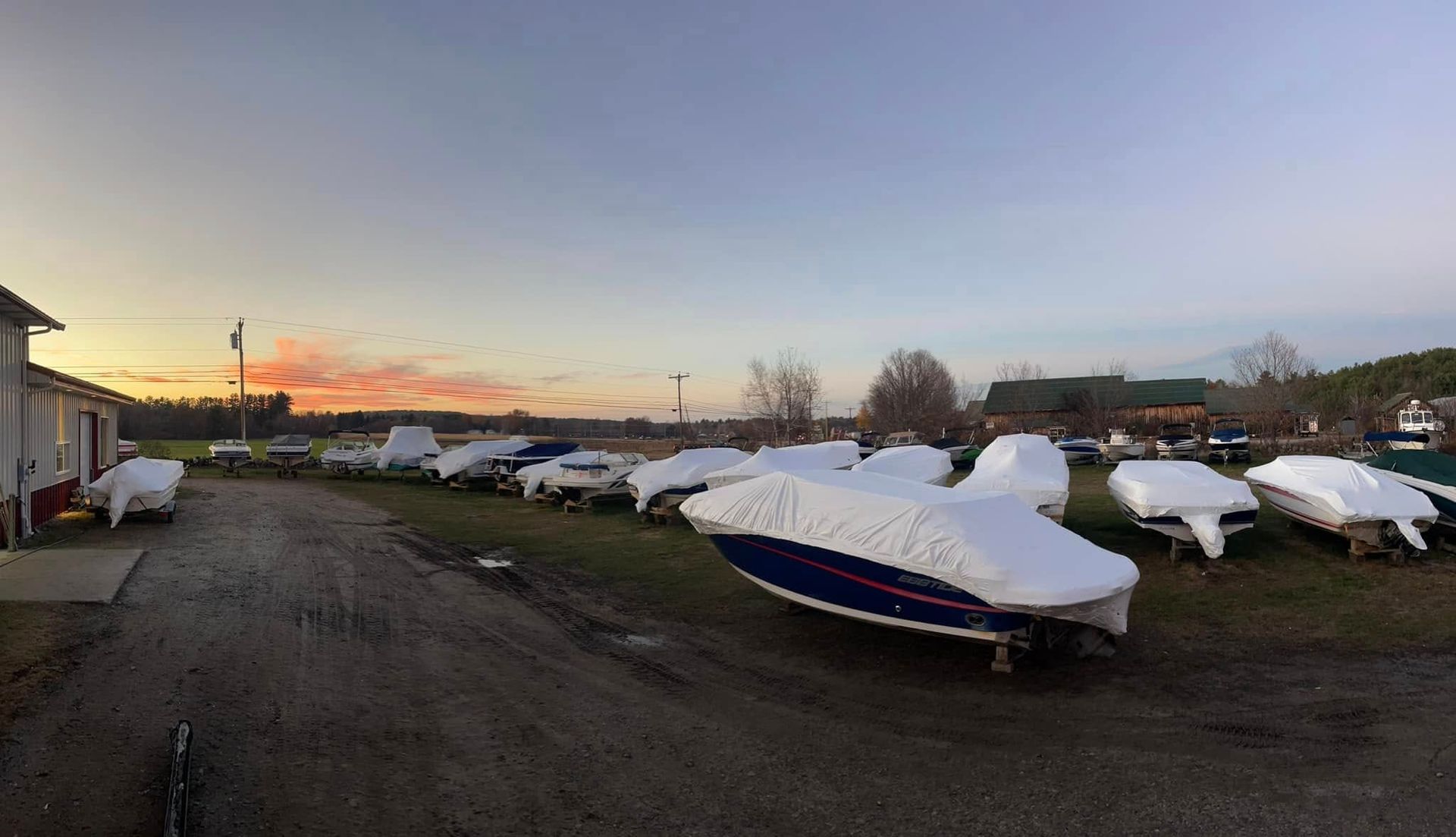 A lot of boats are covered in white covers in a parking lot.