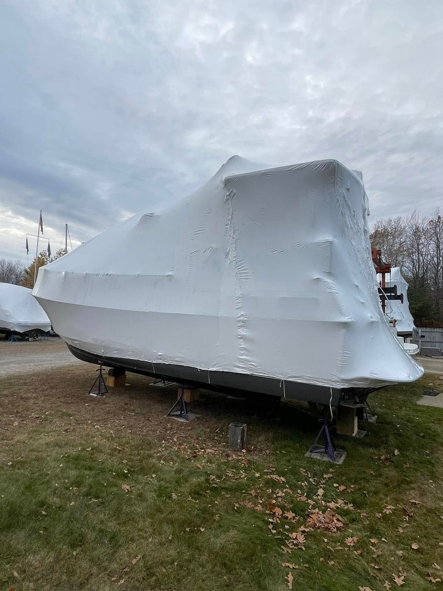 A boat is wrapped in plastic and sitting in the grass.