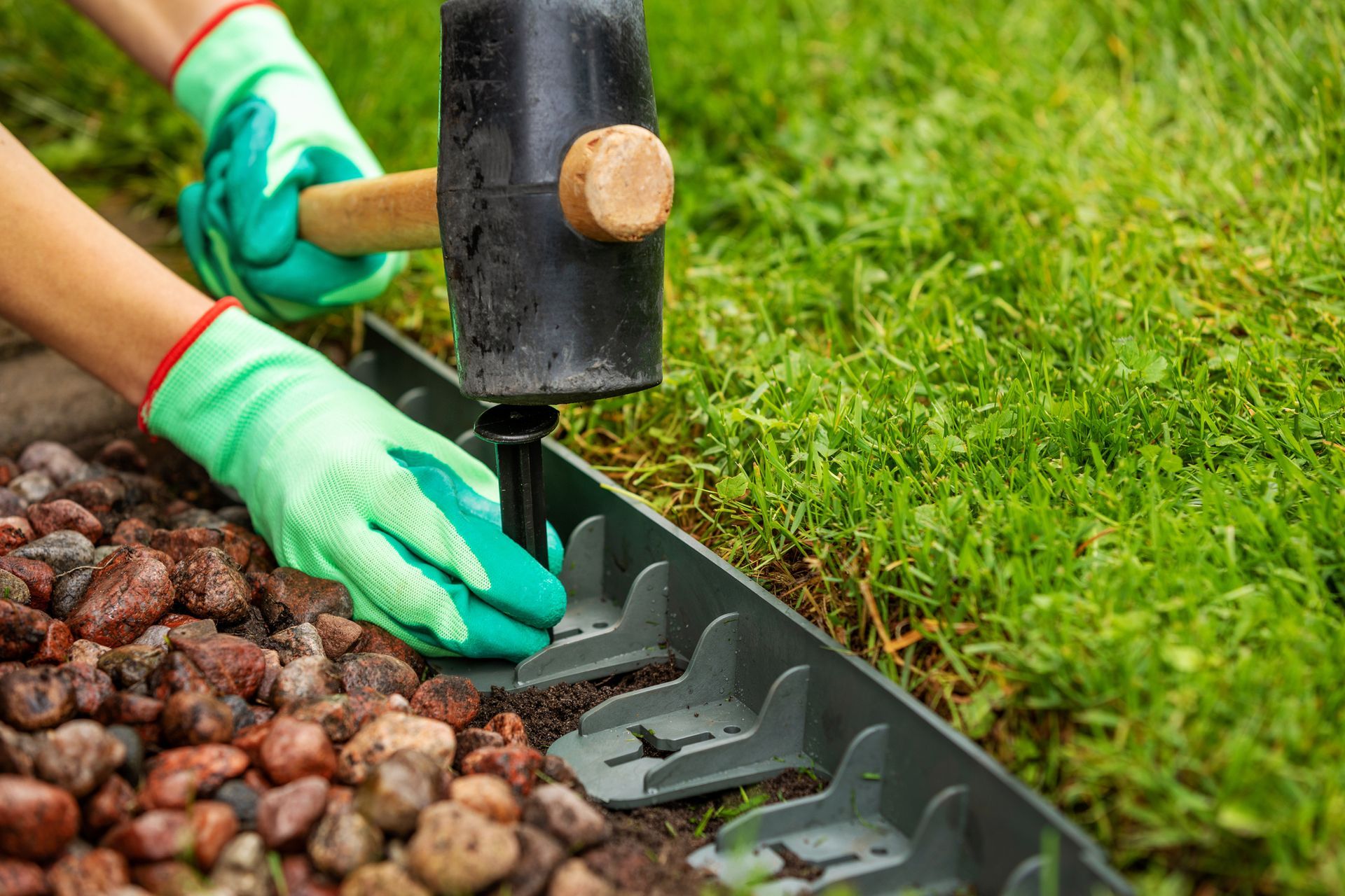 a person wearing green gloves is using a hammer to install a lawn edging