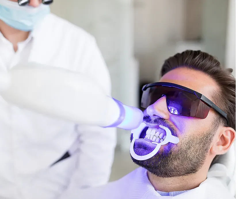 A man with a beard is getting his teeth whitened by a dentist.