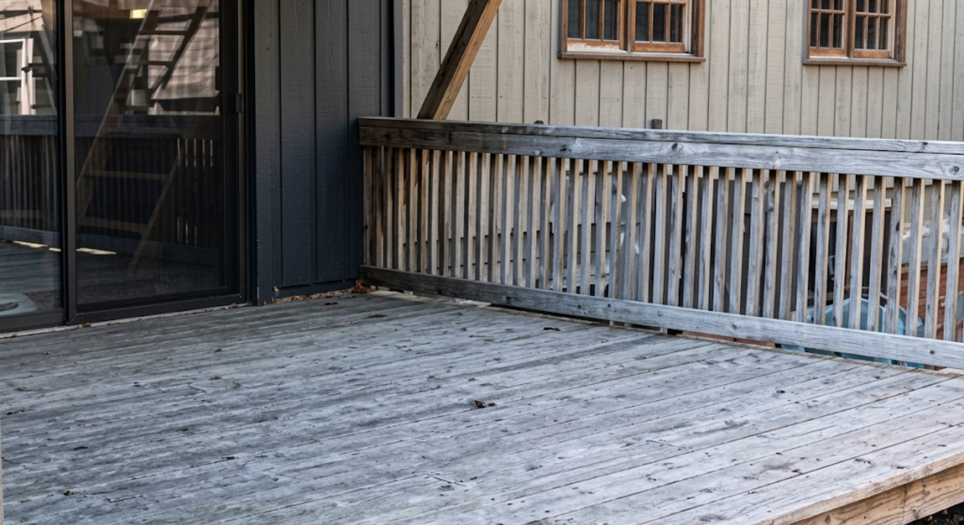 Weathered wooden deck beside a black gate and railing in front of a gray house exterior