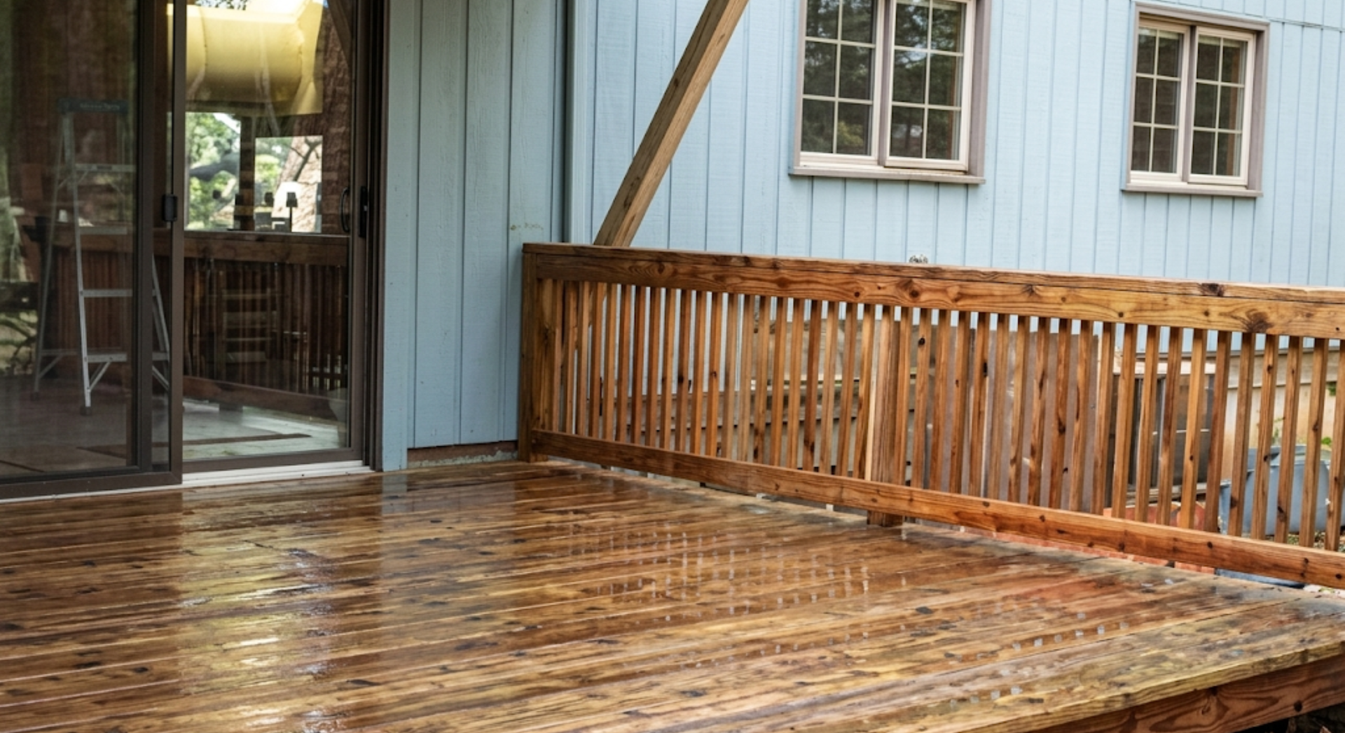 Wooden deck with railing beside a light blue house and sliding glass door