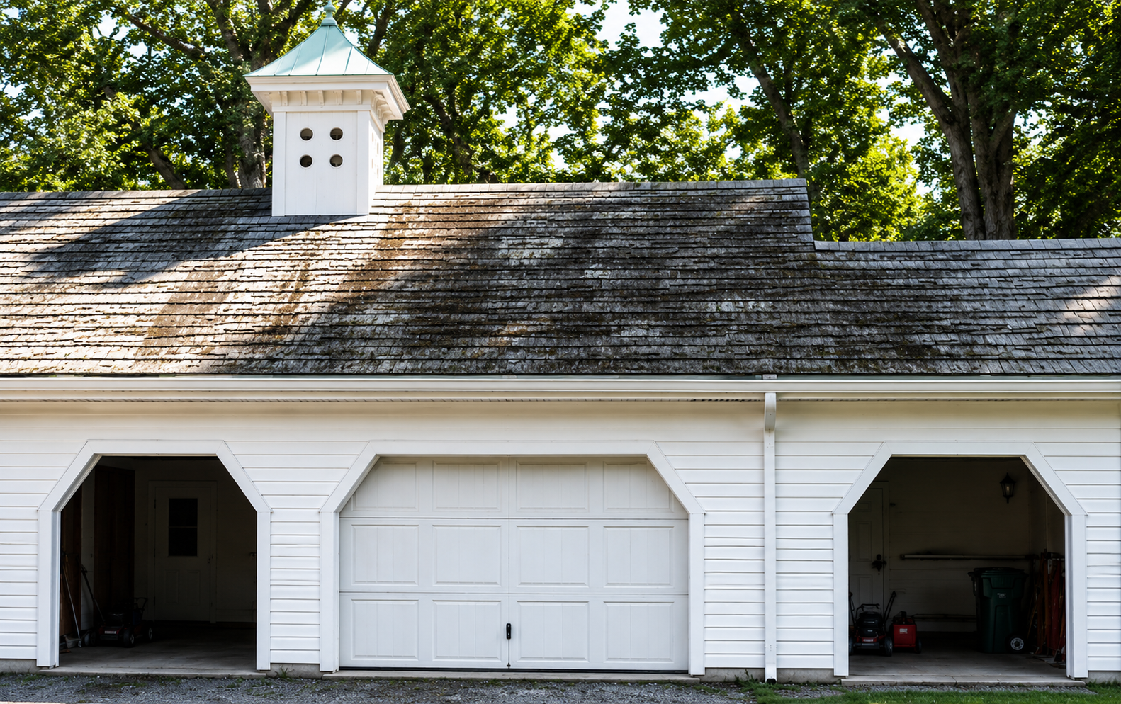 White three-bay garage with a cupola, two open side bays, and one closed center door under trees
