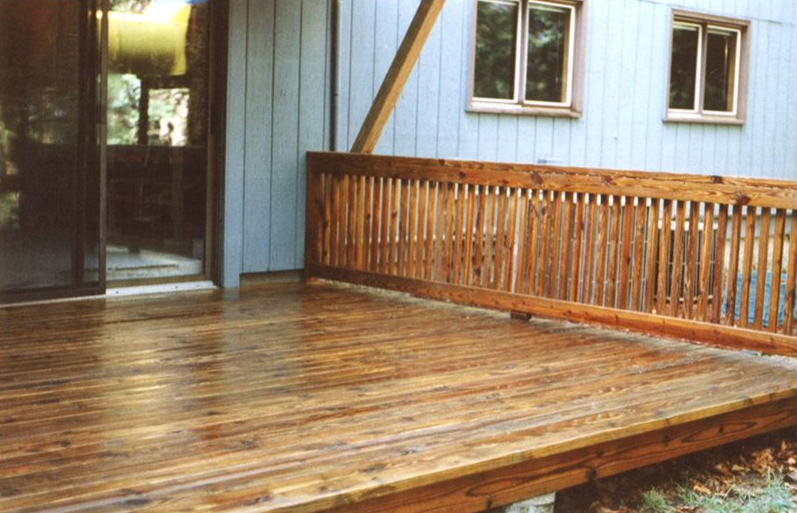 Wooden deck outside a blue house with a railing and sliding glass door