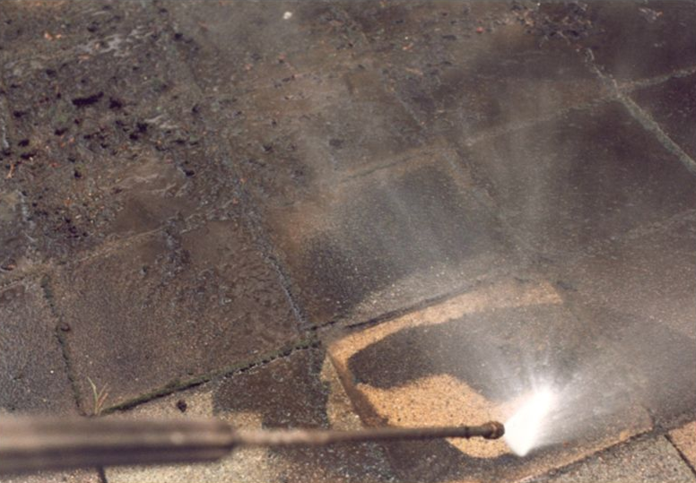 Roof being pressure washed, with water spraying across dark shingles and a bright reflection