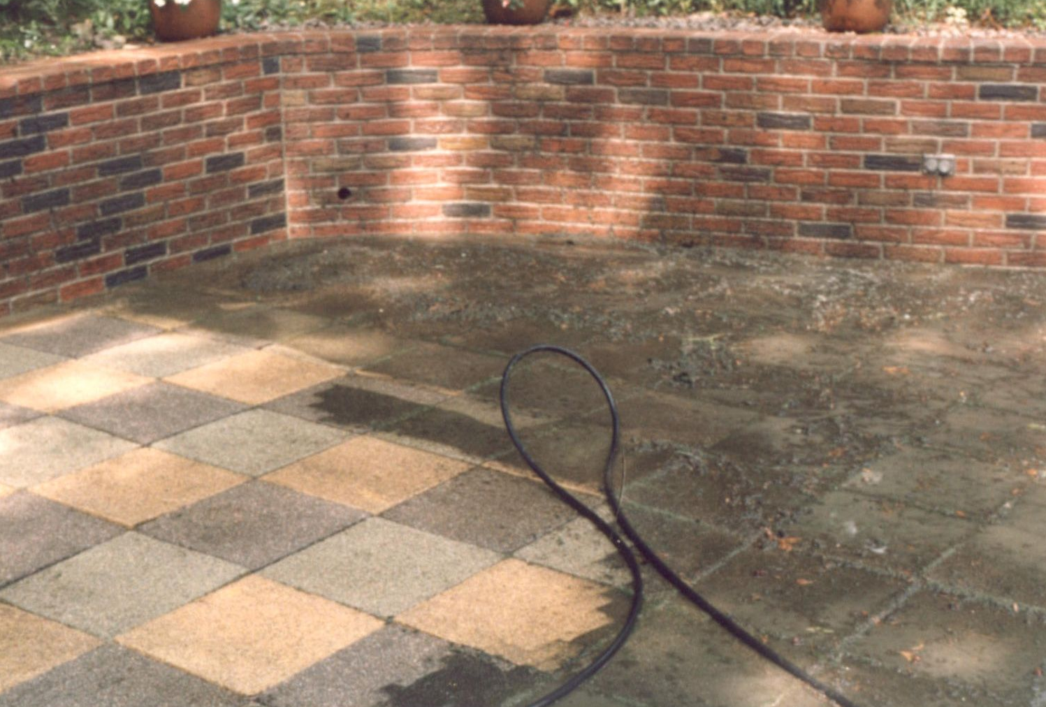 Brick patio with curved brick wall and a garden hose on sunlit stone tiles