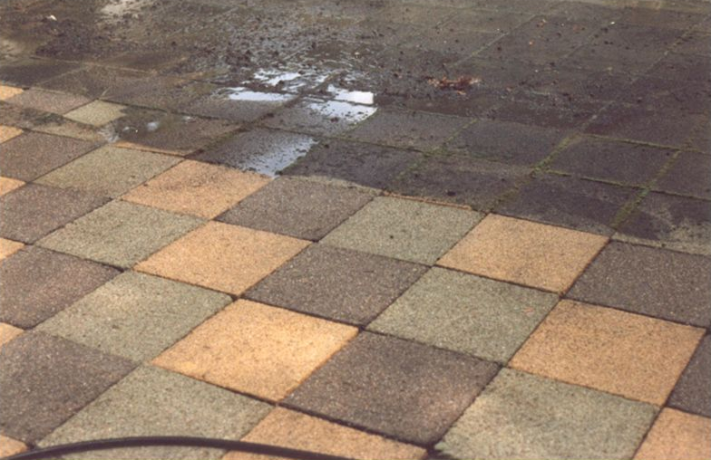 Wet checkerboard pavement tiles with puddles and dark ground at the top edge