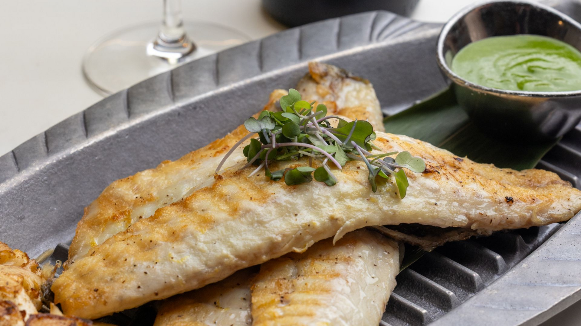Grilled fish fillets on a decorative platter, with a green sauce in a small bowl.