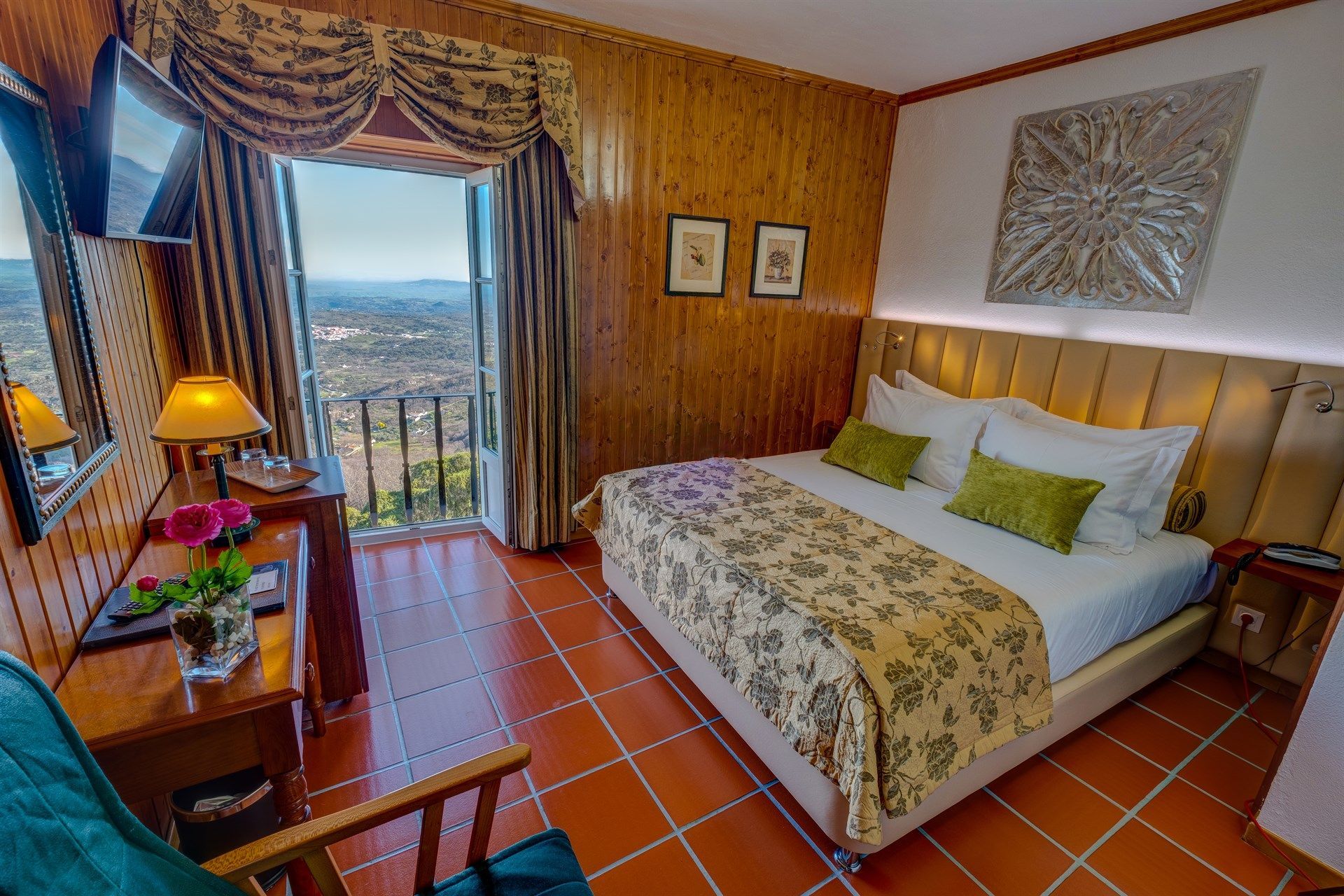 Um quarto de hotel com uma cama grande, escrivaninha, cadeira e televisão. Hotel El Rei Dom Manuel