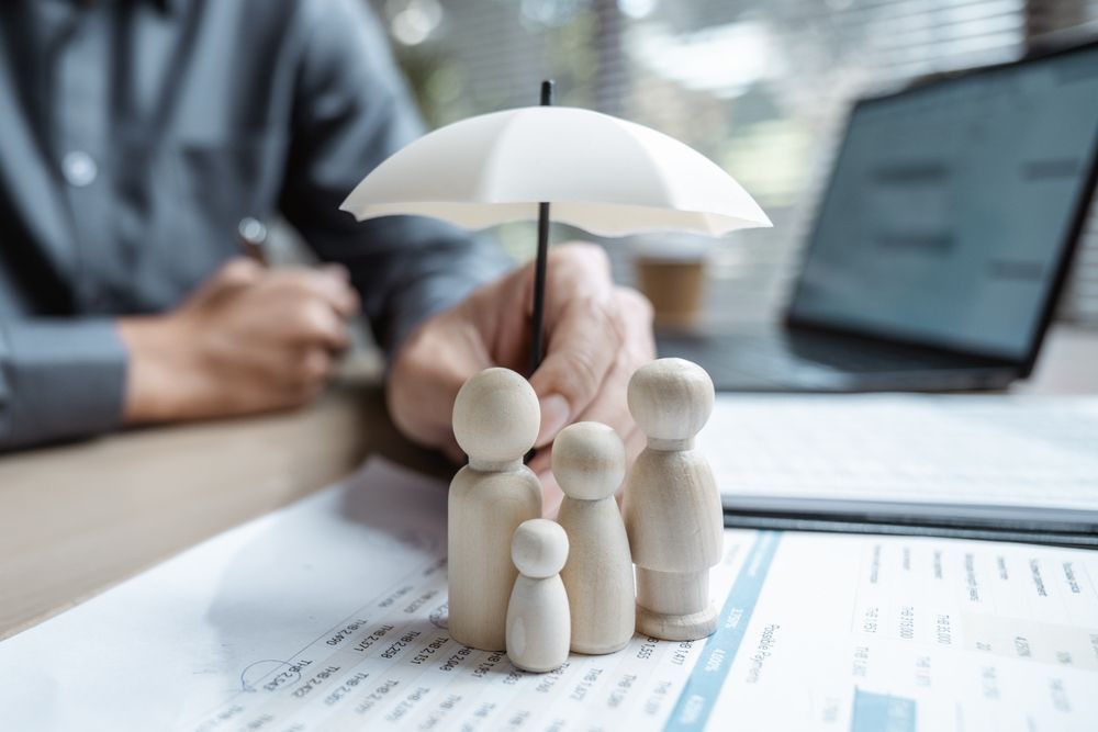 Small wooden family figures under a white umbrella on paperwork beside a laptop